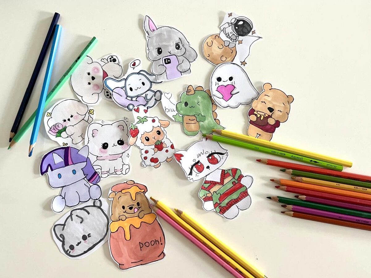 На картинке — лист бумаги с яркими детскими рисунками. Рядом разбросаны цветные карандаши, некоторые с затёртыми концами. Всё выглядит живо и по-доброму, передаёт атмосферу творчества и беззаботного детства.