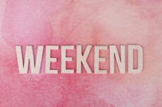 Минималистичная картинка на нежно-розовом акварельном фоне. В центре крупными деревянными буквами выложено слово «WEEKEND». Композиция светлая, спокойная и праздничная.