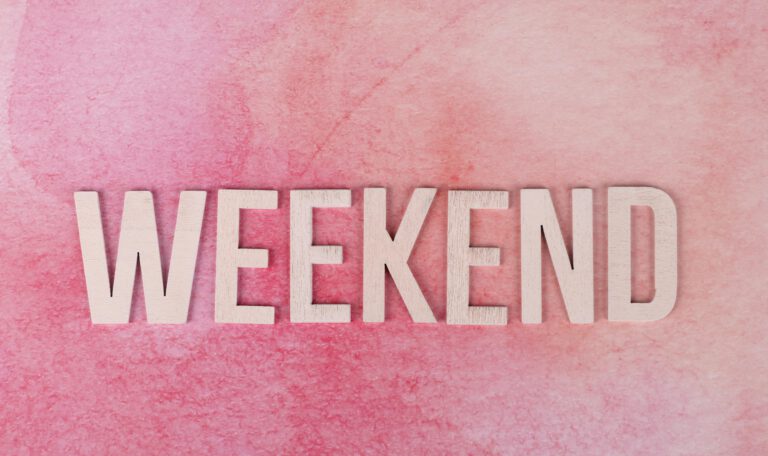 Минималистичная картинка на нежно-розовом акварельном фоне. В центре крупными деревянными буквами выложено слово «WEEKEND». Композиция светлая, спокойная и праздничная.
