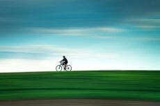 Велосипед в Лейпциге: человек едет на велосипеде по зеленому полю на фоне голубого неба с эффектом размытия движения