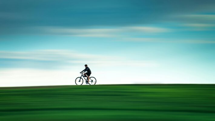 Велосипед в Лейпциге: человек едет на велосипеде по зеленому полю на фоне голубого неба с эффектом размытия движения