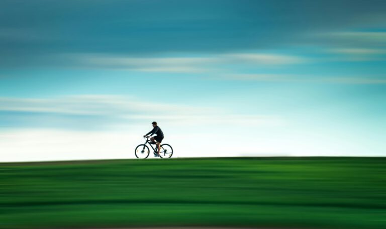 Велосипед в Лейпциге: человек едет на велосипеде по зеленому полю на фоне голубого неба с эффектом размытия движения