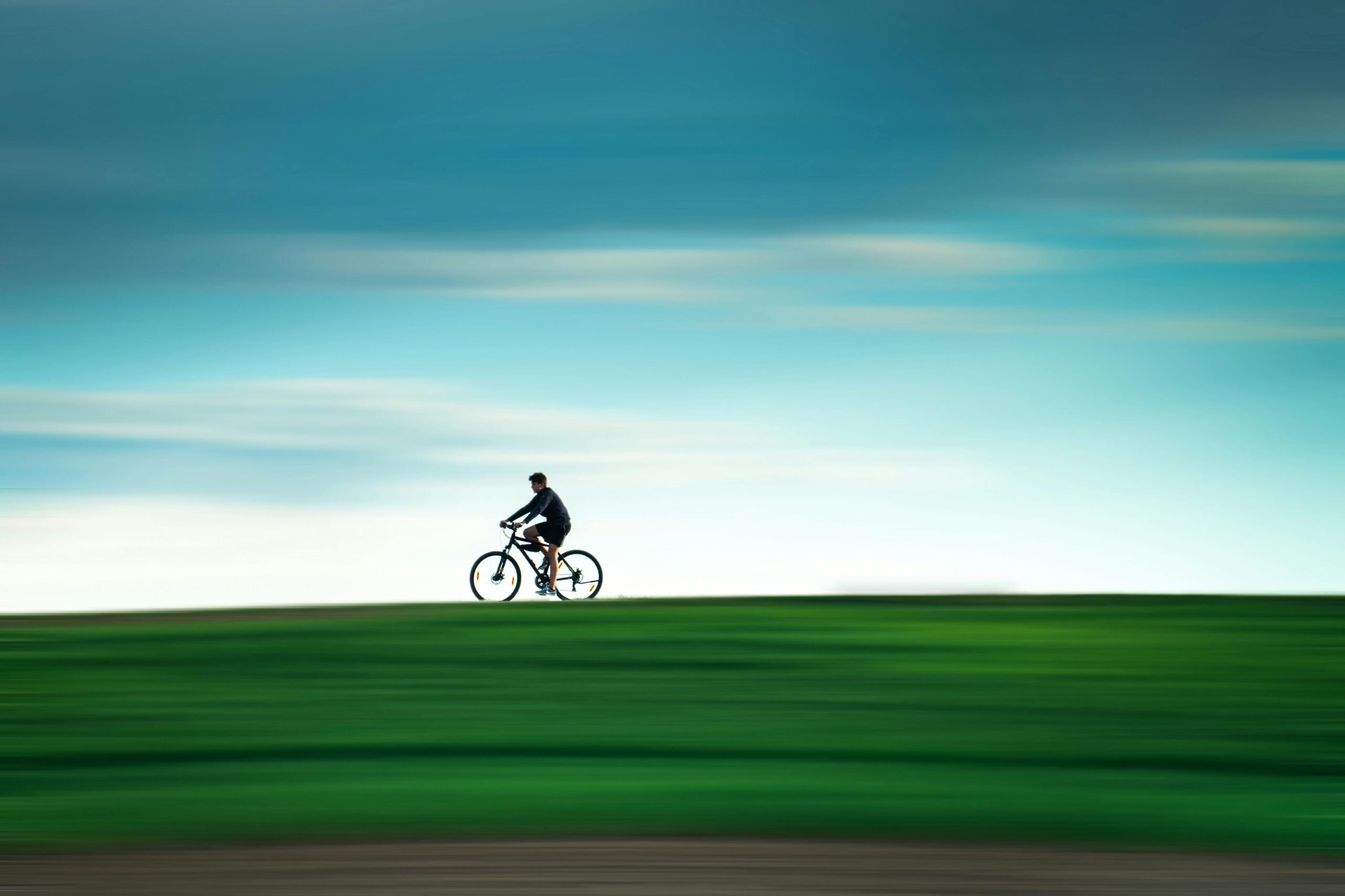 Велосипед в Лейпциге: человек едет на велосипеде по зеленому полю на фоне голубого неба с эффектом размытия движения