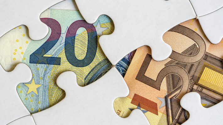 Купюры евро под фрагментами пазла как символ нестабильности потребительских настроений и поиска экономических решений в условиях кризиса