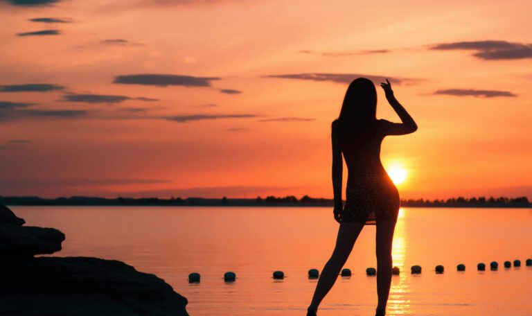 Силуэт девушки на фоне золотого заката у моря — символ безмятежности и спокойствия в одной из самых безопасных стран 2026 года