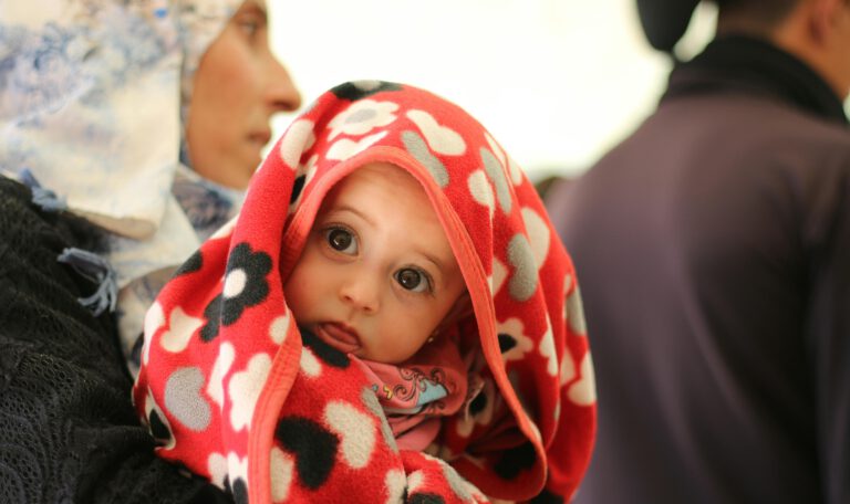 Проницательный взгляд ребенка-беженца: Жизнь за кадром миграционной статистики. Это пронзительное изображение запечатлело момент из жизни маленького человека, чья судьба неразрывно связана с миграционным кризисом. Взгляд этого ребенка, устремленный прямо в объектив, говорит громче любых цифр и отчетов. Закутанный в яркое красное одеяло с узорами, он кажется защищенным, но в то же время невероятно уязвимым. Этот снимок – напоминание о том, что за сухой статистикой «числа прошений об убежище» стоят реальные люди, их истории, страхи и надежды на мирное будущее. В контексте статьи о рекордно низком количестве заявок, это фото заставляет задуматься о цене принятых решений и о том, как меняется миграционная политика на самом деле. Это не просто иллюстрация, а визуальный комментарий к сложной и многогранной теме беженцев в Германии.