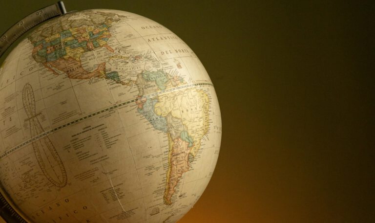 Крупный план винтажного настольного глобуса, на котором видна большая часть Западного полушария. На карте в теплых бежевых и приглушенных пастельных тонах подробно изображены Северная и Южная Америка, а также Атлантический и Тихий океаны. Надписи выполнены на испанском языке. Глобус освещен мягким светом слева, создающим глубокую тень на правой стороне и на темном оливковом фоне, что придает изображению атмосферу классического кабинета. Трамп о позиции Мерца по Ирану