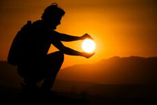 Силуэт человека, который держит светящийся шар солнца в руках на фоне горного заката — метафора управления энергией термоядерного синтеза и создания искусственного солнца