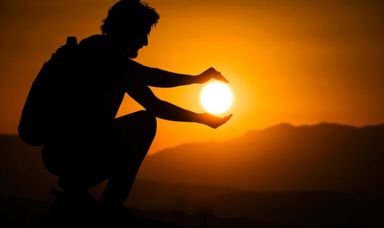 Силуэт человека, который держит светящийся шар солнца в руках на фоне горного заката — метафора управления энергией термоядерного синтеза и создания искусственного солнца