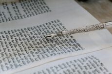 Серебряная указка для Торы (яд) лежит на открытом свитке с текстом на иврите. образовательные центры Яд Вашем
