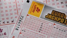Німецькі лотерейні квитки великим планом. На передньому плані розташований заповнений купон Eurojackpot від компанії LOTTO Schleswig-Holstein із закресленими хрестиками числами в ігрових полях. На бланку видно написи німецькою мовою «Hier 5 aus 50 Zahlen ankreuzen» та числовий номер квитка 7264118. На задньому плані розмито видно інші лотерейні картки з червоною сіткою номерів. Лото-мільйонер Чіко