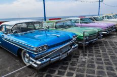 Ряд припаркованных на брусчатке классических американских автомобилей конца 1950-х — начала 1960-х годов на фоне моря. На переднем плане выделяется ярко-синий седан с белой крышей, за ним следуют зеленый и сиреневый автомобили. Машины отделены от зрителя веревочным ограждением. На заднем плане видна набережная с синими фонарными столбами и гирляндами. Купить служебный автомобиль на аукционе в Германии. Ряд припаркованных на брусчатке классических американских автомобилей конца 1950-х — начала 1960-х годов на фоне моря. На переднем плане выделяется ярко-синий седан с белой крышей, за ним следуют зеленый и сиреневый автомобили. Машины отделены от зрителя веревочным ограждением. На заднем плане видна набережная с синими фонарными столбами и гирляндами. Купить служебный автомобиль на аукционе в Германии.