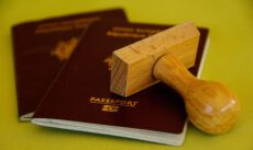 Крупный план на желто-зеленом фоне: деревянный штамп лежит поверх двух темно-бордовых паспортов Французской Республики, на которых золотым тиснением написано PASSEPORT. Перетин кордону податкова. Крупный план на желто-зеленом фоне: деревянный штамп лежит поверх двух темно-бордовых паспортов Французской Республики, на которых золотым тиснением написано PASSEPORT. Перетин кордону податкова.