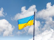 На фото зображено державний прапор України, який майорить на високому флагштоку. Полотнище прапора складається з двох рівних горизонтальних смуг: синьої зверху та жовтої знизу. Флагтсток розташований праворуч і йде вертикально вгору. На тлі видно яскраво-блакитне небо, покрите легкими, пухнастими білими хмарами. Освітлення денне, природне, що підкреслює яскраві кольори прапора. Підтримка вступу України в ЄС у Німеччині. На фото зображено державний прапор України, який майорить на високому флагштоку. Полотнище прапора складається з двох рівних горизонтальних смуг: синьої зверху та жовтої знизу. Флагтсток розташований праворуч і йде вертикально вгору. На тлі видно яскраво-блакитне небо, покрите легкими, пухнастими білими хмарами. Освітлення денне, природне, що підкреслює яскраві кольори прапора. Підтримка вступу України в ЄС у Німеччині.